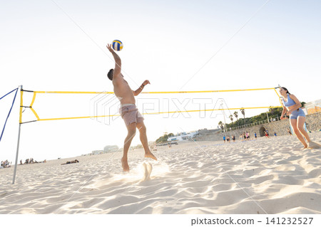 Young man jumping hitting beach volleyball during game Young man jumping hitting beach volleyball during game 141232527