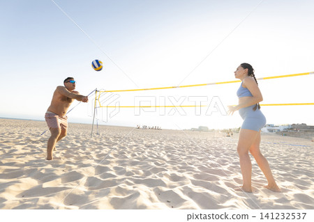 Couple playing beach volleyball on sandy court at sunset Couple playing beach volleyball on sandy court at sunset 141232537
