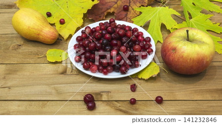 Autumn Still Life. Cranberries on a white plate, autumn leaves and pear apple Autumn Still Life. Cranberries on a white plate, autumn leaves and pear apple 141232846