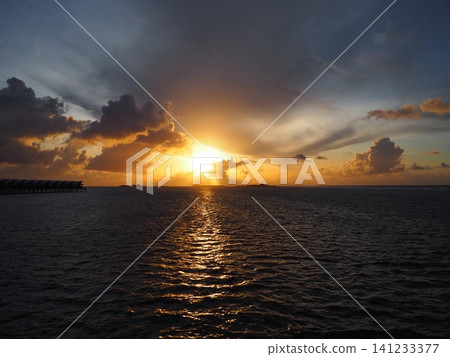 A beautiful sunrise viewed from an overwater villa in the Maldives, with a golden path of light illuminating the surface of the sea. A beautiful sunrise viewed from an overwater villa in the Maldives, with a golden path of light illuminating the surface of the sea. 141233377