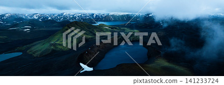 Panoramic view of crater lake in Iceland's Highlands, surrounded by dark volcanic slopes beneath dramatic storm clouds. A remote and breathtaking volcanic landscape. 141233724