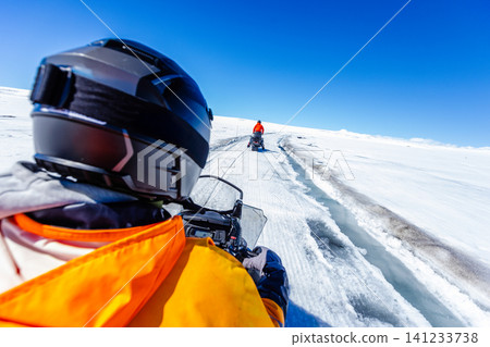 First-person view of a snowmobile tour across a vast Icelandic glacier. Adventure travel through pristine snowfields beneath a dramatic blue sky with wispy clouds in Iceland. First-person view of a snowmobile tour across a vast Icelandic glacier. Adventure travel through pristine snowfields beneath a dramatic blue sky with wispy clouds in Iceland. 141233738