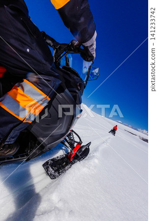 Close-up perspective of a snowmobile rider crossing a pristine Icelandic glacier, following another snowmobile across untouched snow beneath a vivid blue sky during a winter adventure. Close-up perspective of a snowmobile rider crossing a pristine Icelandic glacier, following another snowmobile across untouched snow beneath a vivid blue sky during a winter adventure. 141233742