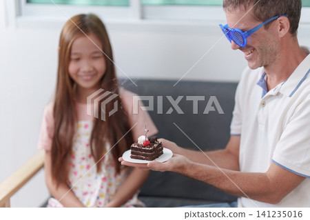 Happy father giving birthday cake to daughter at home celebration Happy father giving birthday cake to daughter at home celebration 141235016