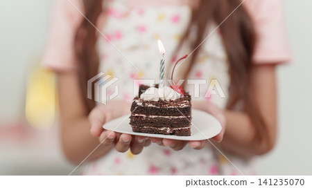 Cropped hands of child holding slice of chocolate birthday cake with lit candle Cropped hands of child holding slice of chocolate birthday cake with lit candle 141235070