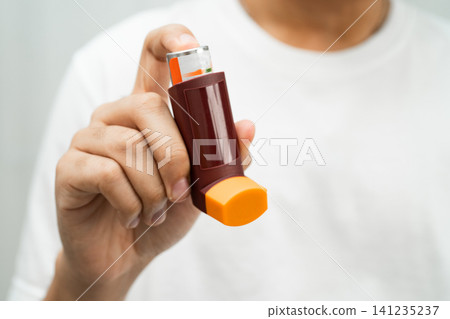 Asthma and chronic obstructive pulmonary disease COPD, Asian young man using metered dose inhaler MDI. Asthma and chronic obstructive pulmonary disease COPD, Asian young man using metered dose inhaler MDI. 141235237