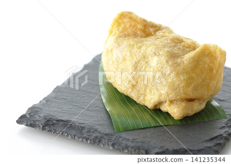 Inari sushi on a slate plate photographed against a white background. 141235344