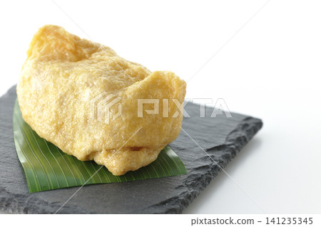 Inari sushi on a slate plate photographed against a white background. 141235345