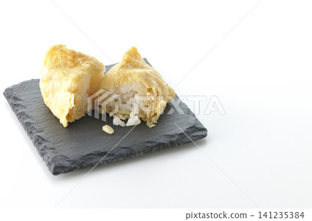 Inari sushi on a slate plate photographed against a white background. 141235384
