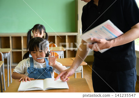 一位男老師正在教室裡看著一位女小學生學習。 一位男老師正在教室裡看著一位女小學生學習。 141235547