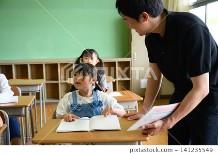 一位男老師正在教室裡看著一位女小學生學習。 一位男老師正在教室裡看著一位女小學生學習。 141235549