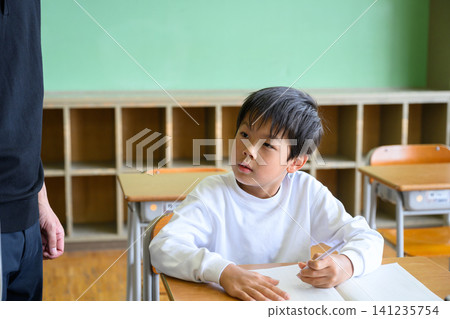 一位男老師正在教室裡看著一位女小學生學習。 一位男老師正在教室裡看著一位女小學生學習。 141235754