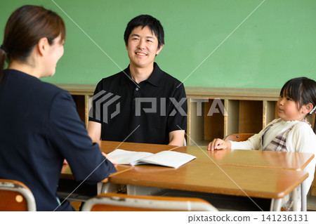 A female teacher, a father, and an elementary school girl are having a friendly and cheerful three-way meeting in a classroom (career guidance/tutoring). A female teacher, a father, and an elementary school girl are having a friendly and cheerful three-way meeting in a classroom (career guidance/tutoring). 141236131