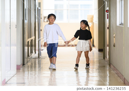 A boy and a girl, both elementary school students, walking down the school corridor hand in hand. 141236235