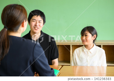 一位女教師、一位父親和一位小學生在教室裡進行了一場友好而愉快的三方會面(職業指導/輔導)。 一位女教師、一位父親和一位小學生在教室裡進行了一場友好而愉快的三方會面(職業指導/輔導)。 141236383