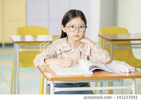 Asian schoolgirl doing homework with glasses in a bright classroom Asian schoolgirl doing homework with glasses in a bright classroom 141237091
