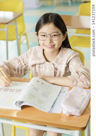 Asian schoolgirl doing homework with glasses in a bright classroom Asian schoolgirl doing homework with glasses in a bright classroom 141237104