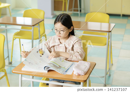 Asian schoolgirl doing homework with glasses in a bright classroom Asian schoolgirl doing homework with glasses in a bright classroom 141237107