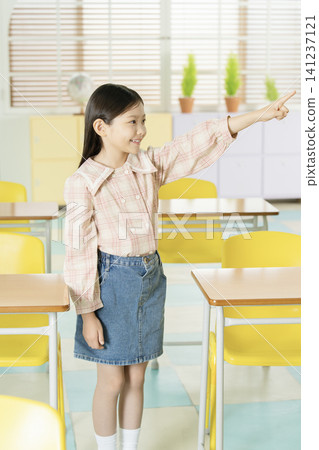Elementary schoolgirl standing in a classroom with a white backpack Elementary schoolgirl standing in a classroom with a white backpack 141237121