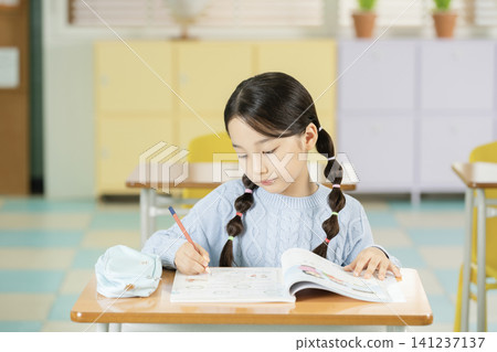 Asian elementary schoolgirl with braided hair studying at a classroom desk Asian elementary schoolgirl with braided hair studying at a classroom desk 141237137