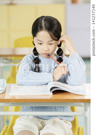 Asian elementary schoolgirl with braided hair studying at a classroom desk Asian elementary schoolgirl with braided hair studying at a classroom desk 141237140