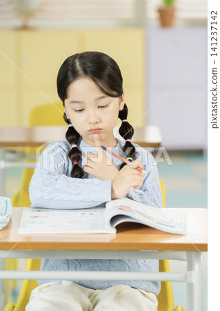 Young schoolgirl raising her hand while studying in class Young schoolgirl raising her hand while studying in class 141237142