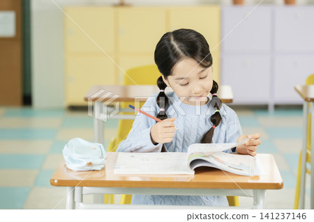 Asian elementary schoolgirl with braided hair studying at a classroom desk Asian elementary schoolgirl with braided hair studying at a classroom desk 141237146