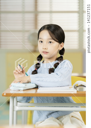 Elementary student writing in a textbook at her desk 141237151