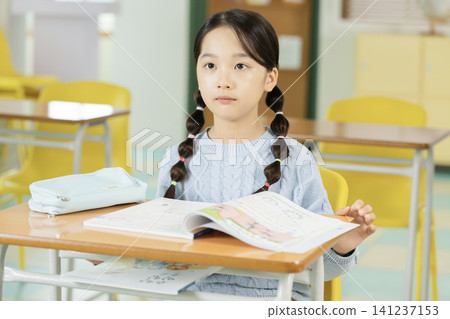 Asian elementary schoolgirl with braided hair studying at a classroom desk Asian elementary schoolgirl with braided hair studying at a classroom desk 141237153
