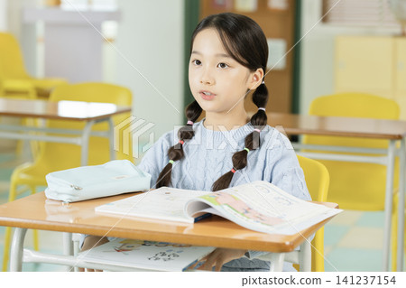 Young schoolgirl raising her hand while studying in class 141237154