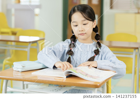 Elementary student writing in a textbook at her desk Elementary student writing in a textbook at her desk 141237155
