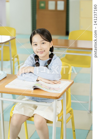 Schoolgirl with backpack smiling in a bright classroom Schoolgirl with backpack smiling in a bright classroom 141237160