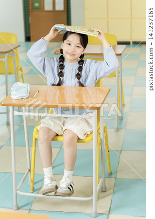 Asian elementary schoolgirl with braided hair studying at a classroom desk Asian elementary schoolgirl with braided hair studying at a classroom desk 141237165