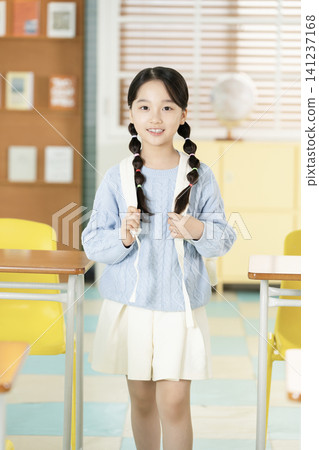 Schoolgirl with backpack smiling in a bright classroom Schoolgirl with backpack smiling in a bright classroom 141237168