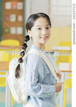 Schoolgirl with backpack smiling in a bright classroom Schoolgirl with backpack smiling in a bright classroom 141237172