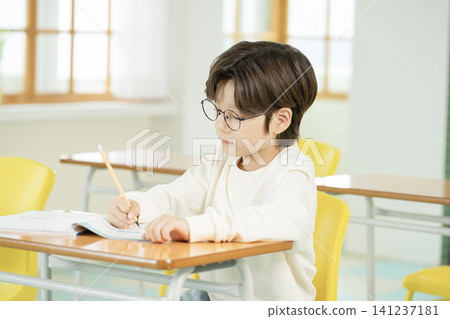 Asian elementary schoolboy with glasses studying in a classroom Asian elementary schoolboy with glasses studying in a classroom 141237181