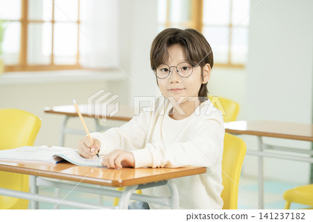 Young schoolboy writing in a textbook at a classroom desk 141237182