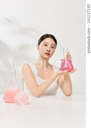 Young Asian woman presenting pink cosmetic formula in glass laboratory flasks Young Asian woman presenting pink cosmetic formula in glass laboratory flasks 141237195