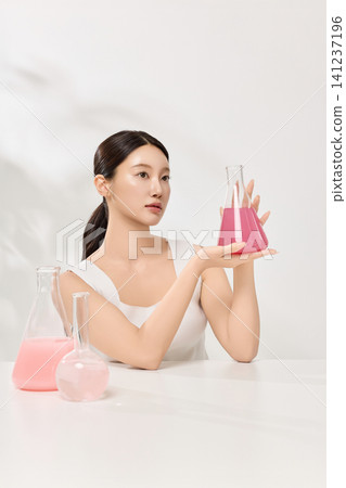 Beauty model holding beakers with pink skincare liquid in a clean studio Beauty model holding beakers with pink skincare liquid in a clean studio 141237196