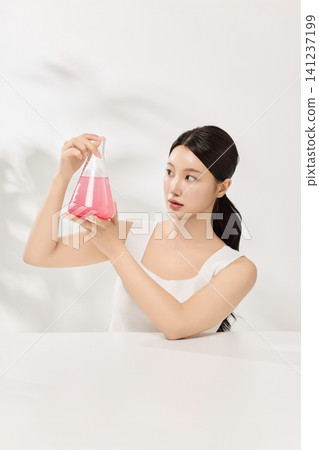 Young Asian woman presenting pink cosmetic formula in glass laboratory flasks Young Asian woman presenting pink cosmetic formula in glass laboratory flasks 141237199