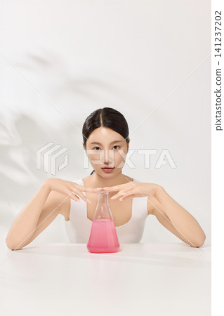 Beauty model holding beakers with pink skincare liquid in a clean studio Beauty model holding beakers with pink skincare liquid in a clean studio 141237202