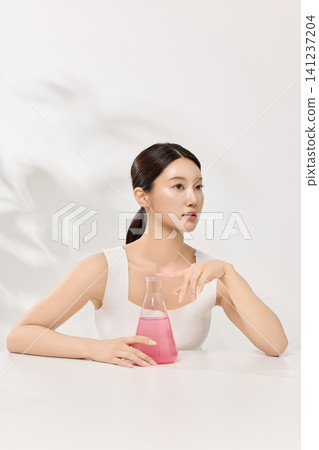 Young Asian woman presenting pink cosmetic formula in glass laboratory flasks Young Asian woman presenting pink cosmetic formula in glass laboratory flasks 141237204