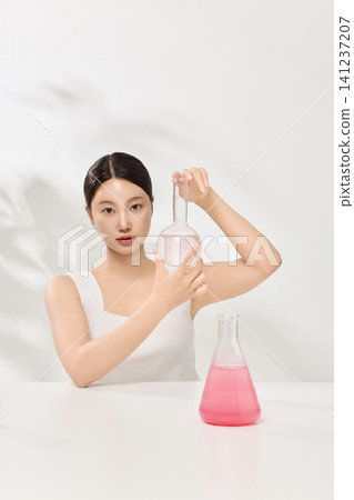 Asian woman posing with laboratory glassware and pink beauty serum 141237207
