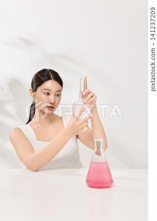 Beauty model holding beakers with pink skincare liquid in a clean studio Beauty model holding beakers with pink skincare liquid in a clean studio 141237209