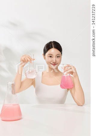 Asian woman posing with laboratory glassware and pink beauty serum 141237219