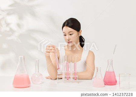 Young Asian woman presenting pink cosmetic formula in glass laboratory flasks Young Asian woman presenting pink cosmetic formula in glass laboratory flasks 141237228