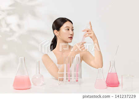 Beauty model holding beakers with pink skincare liquid in a clean studio 141237229