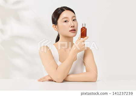 Asian woman smiling with an amber beauty product bottle Asian woman smiling with an amber beauty product bottle 141237239