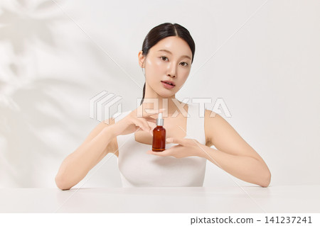 Beauty model posing with a brown cosmetic bottle in a clean studio 141237241