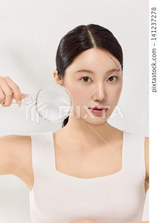 Asian model holding a magnifying glass for facial skin analysis Asian model holding a magnifying glass for facial skin analysis 141237278